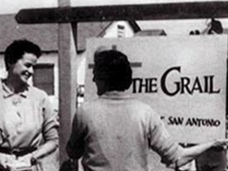 Black and white photo of two people in front of the historic Grail sign
